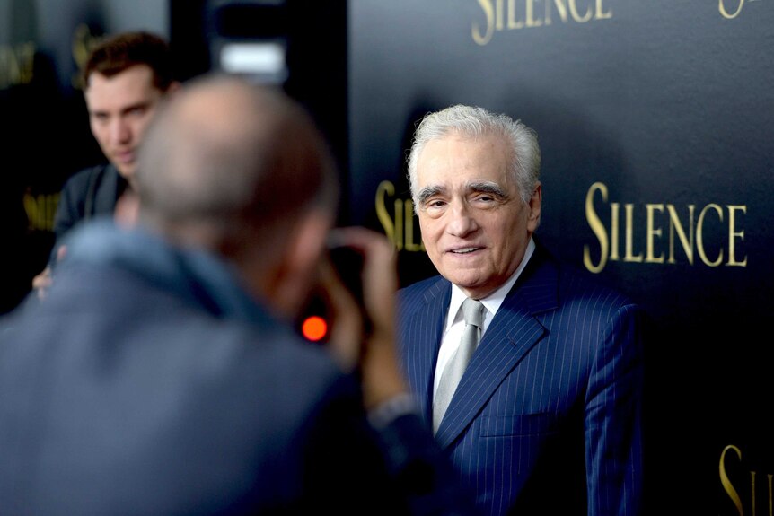 Director Martin Scorsese stands in front of a sign for his film Silence as photographers surround him