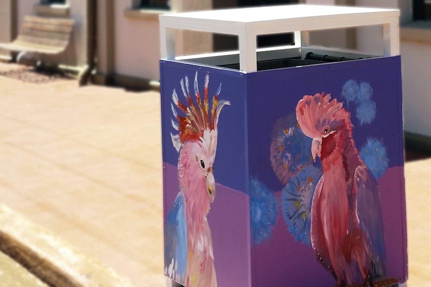 A bin painted with a mural of a pink and grey galah installed on the street