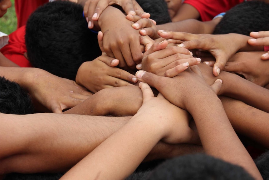 Hands coming together in the centre of a circle of young rugby players.