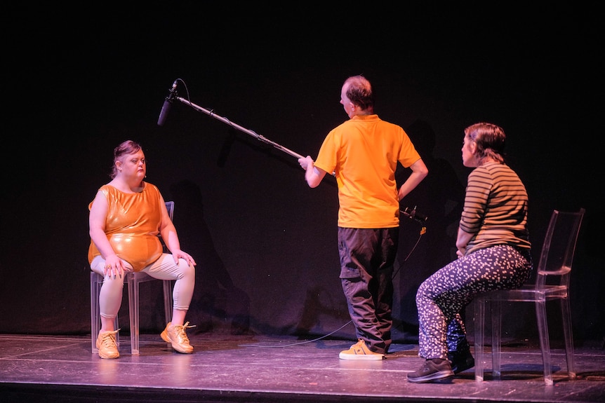 Three people on stage, one holding a boom mic.