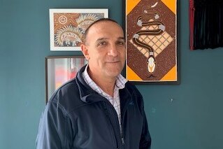 A man with short dark hair in front of Indigenous paintings