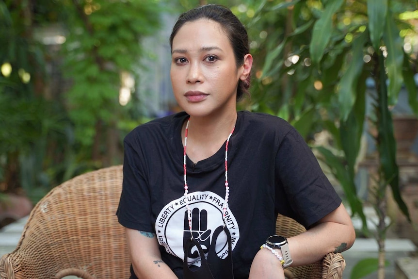 A woman with brown hair and brown eyes wears a black teacher with Liberty Equality Fraternity written on it as she sit