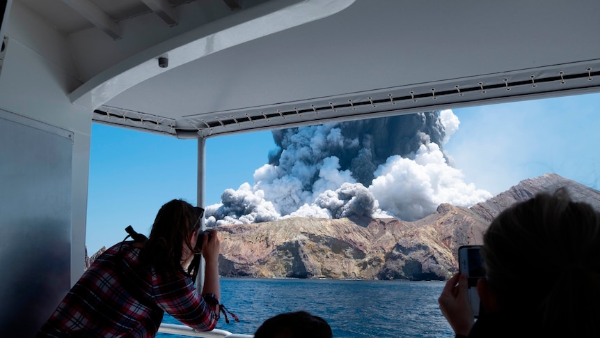 A woman takes a photo from a boat of an erupting volcano
