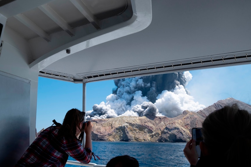 A woman takes a photo from a boat of an erupting volcano