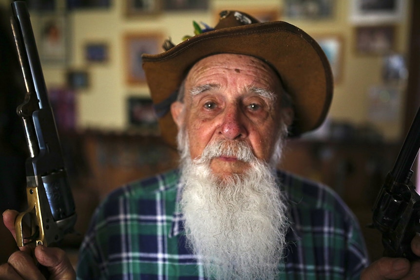 old man iwth scrappy akubra hat and a grey beard holds a rifle.