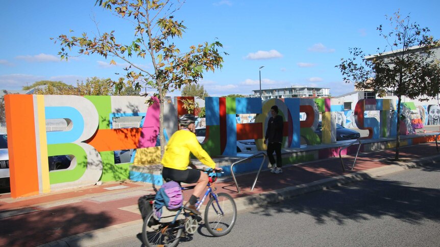 A cyclist rides past large colourful letters spelling out 'Beaufort St'.