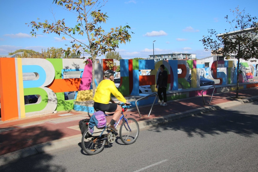A cyclist rides past large colourful letters spelling out 'Beaufort St'.