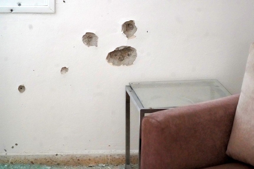Several large bullet holes in a wall, near a sofa