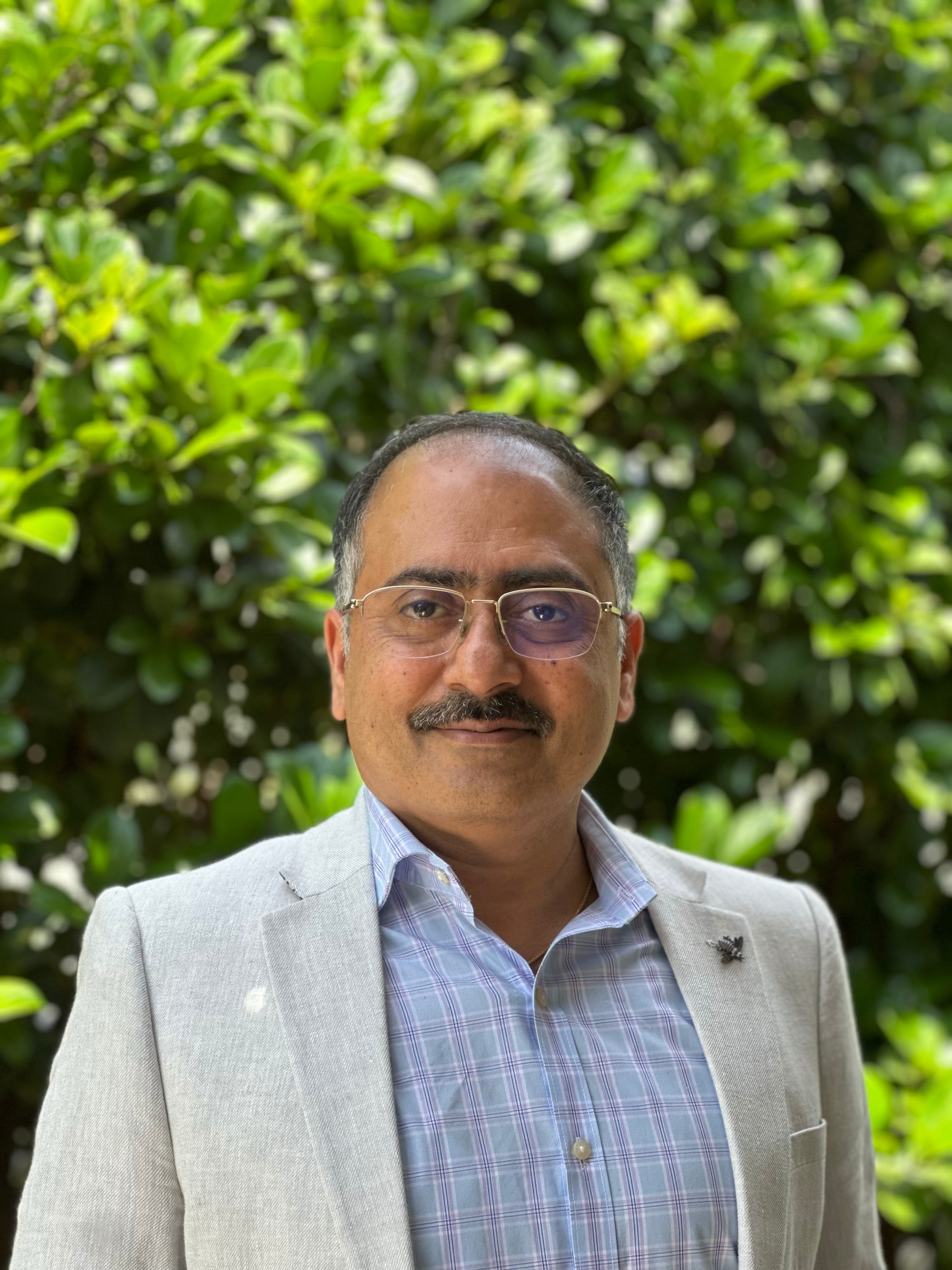 Hombre indio con gafas de metal, bigote canoso y pelo blanco en las sienes.