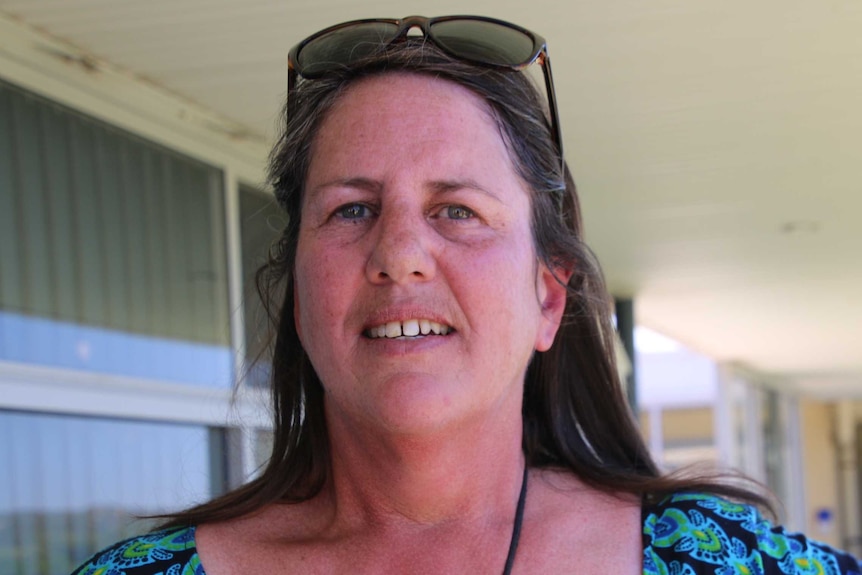 A woman wearing a blue dress and sunglasses on her head smiles at the camera