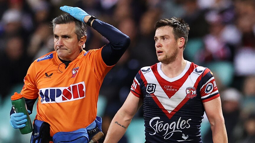 A Sydney Roosters trainer pats his head to signal a head injury to Luke Keary during an NRL game.