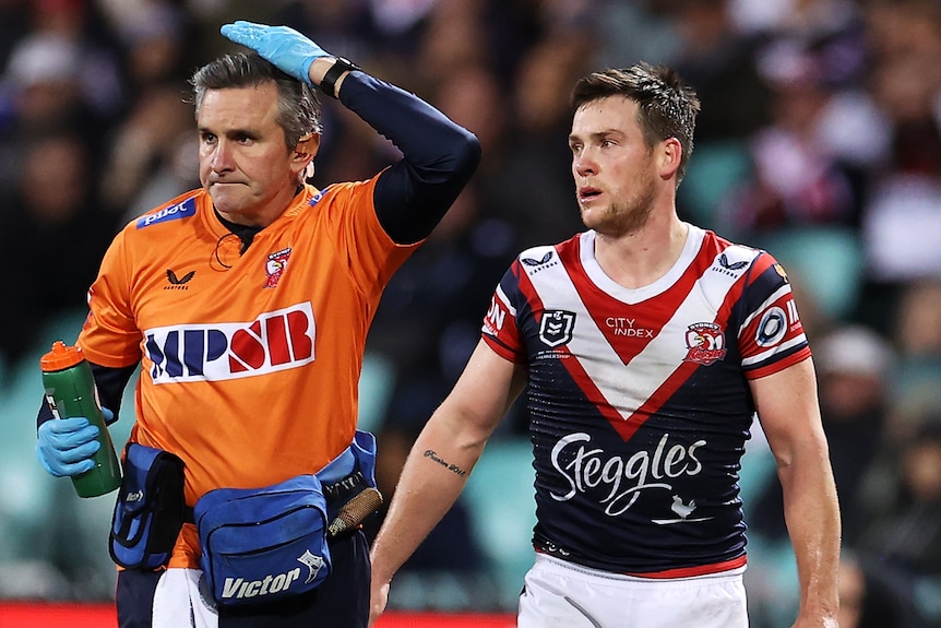 A Sydney Roosters trainer pats his head to signal a head injury to Luke Keary during an NRL game.