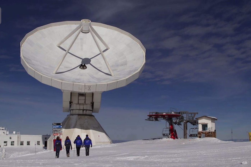 A giant telescope with people walking in front on snow.