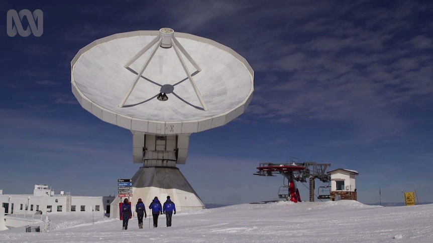 A giant telescope with people walking in front on snow.