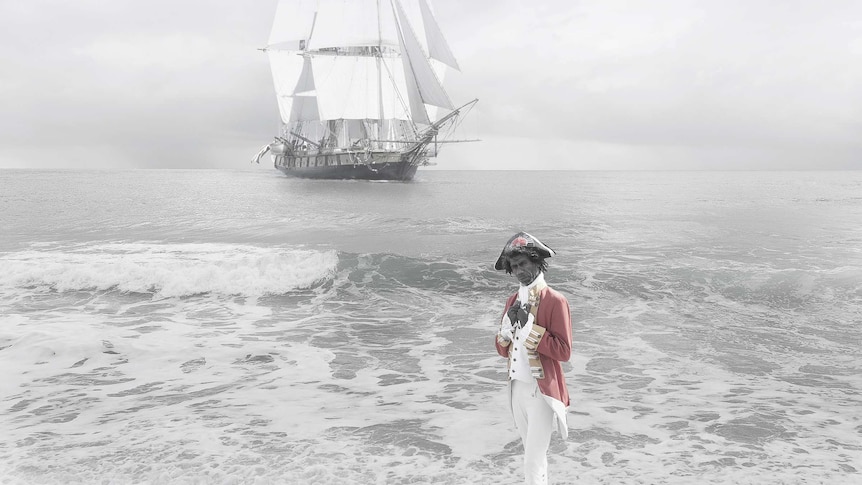 A photograph by Michael Cook showing an Aboriginal man in traditional European dress in front of the ship Endeavour.