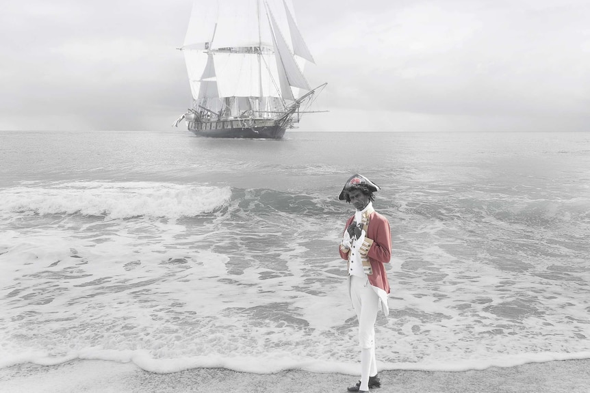 A photograph by Michael Cook showing an Aboriginal man in traditional European dress in front of the ship Endeavour.