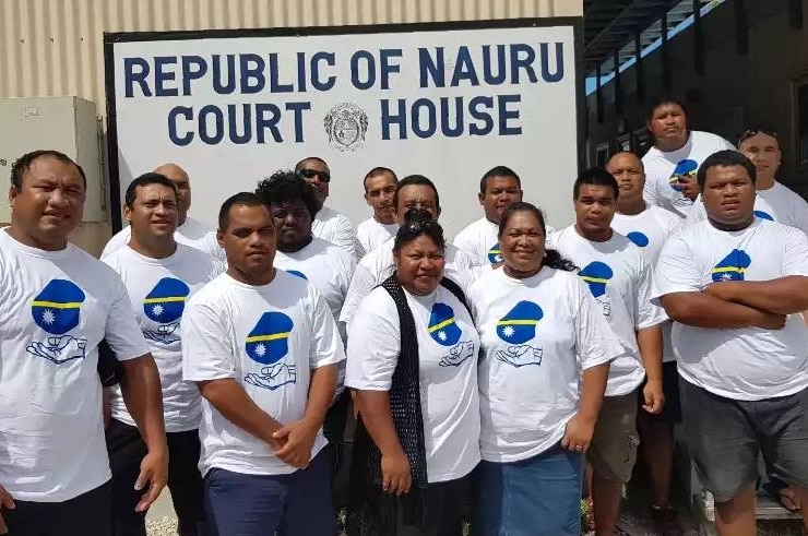 A group of Nauruan men and women wear matching white t-shirts in front of the court room.