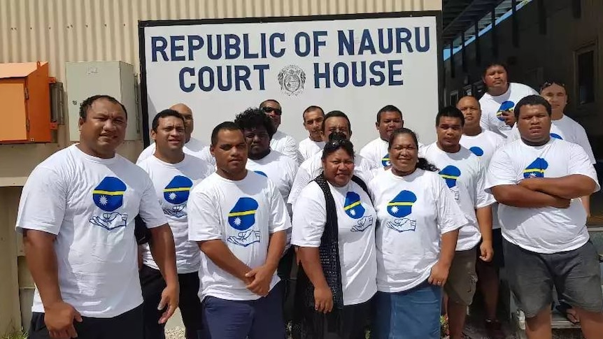 A group of Nauruan men and women wear matching white t-shirts in front of the court room.