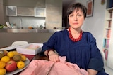 Cecilia Anthony sitting in her kitchen with a dried rose on pink wrapping paper on the dining table