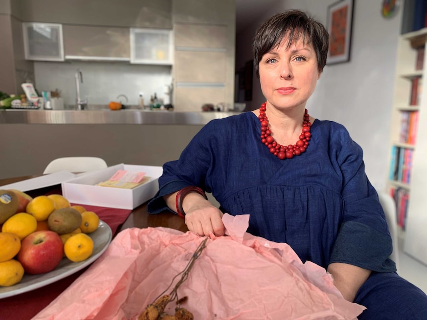 Cecilia Anthony sitting in her kitchen with a dried rose on pink wrapping paper on the dining table