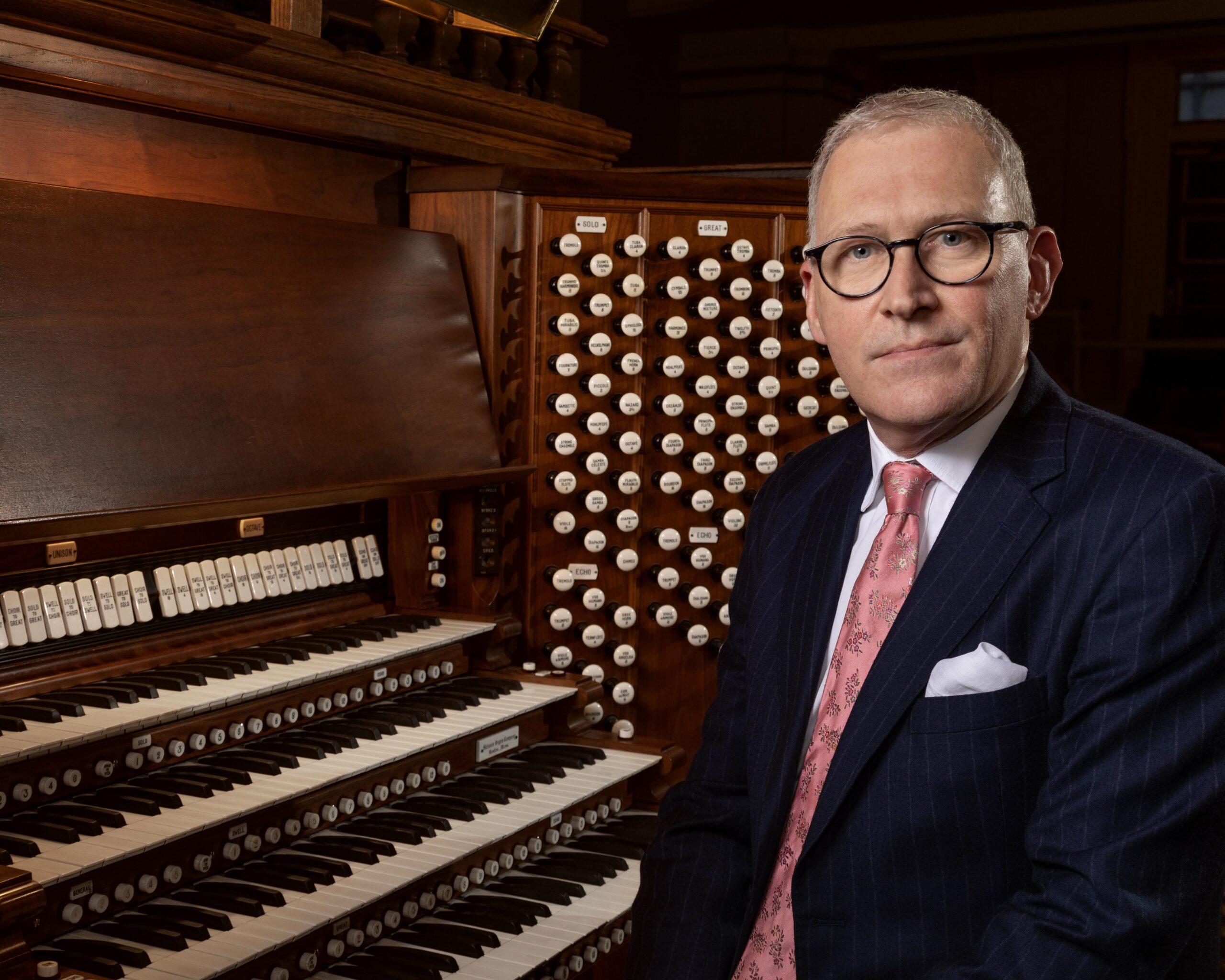 A close-up shot of organist James O&#x27;Donnell in a suit with pocket hankerchief, seated at an organ. 