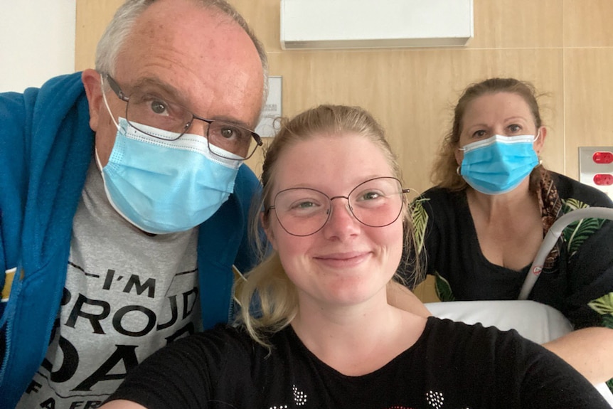 Man and woman wearing facemasks with their daughter who is a hospital patient.