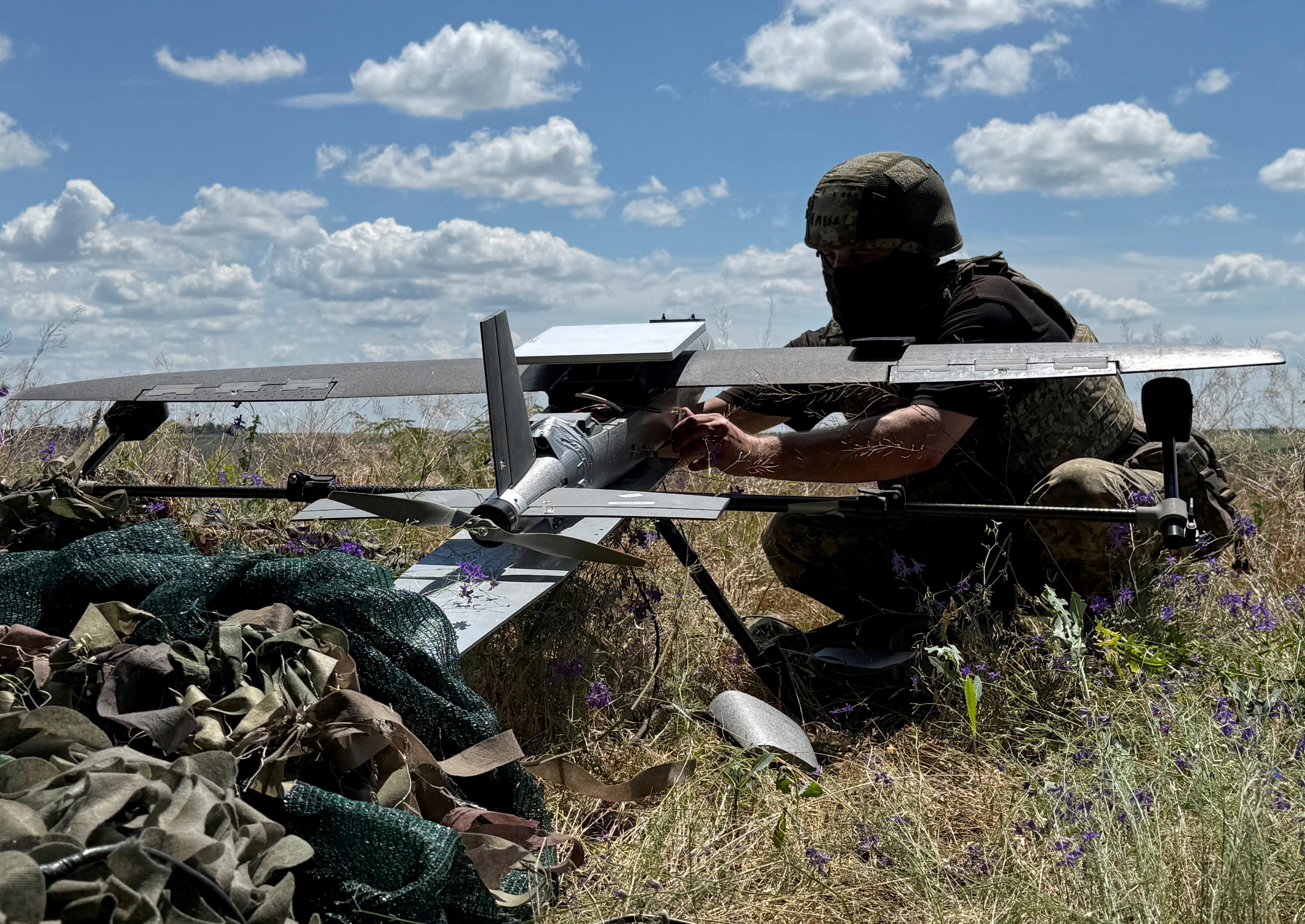 A Ukrainian serviceman is crouching on the ground next to a hornet strike drone, preparing to launch.