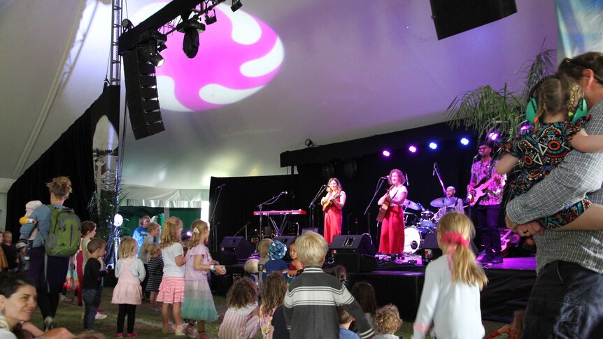 A live band performs in a festival tent to a crowd of dancing children.