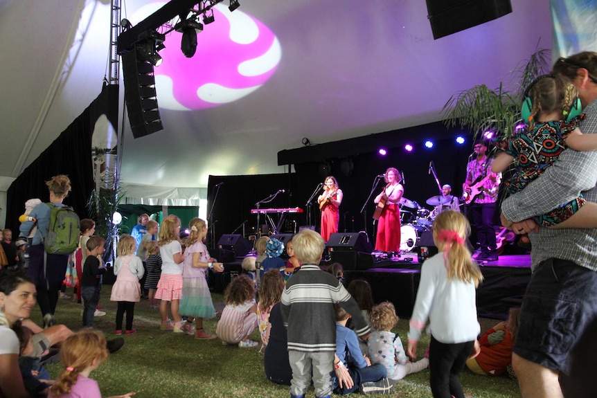 A live band performs in a festival tent to a crowd of dancing children.