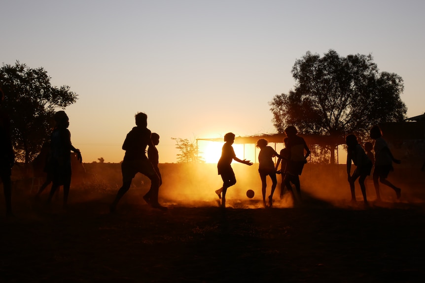 A sunset shot of children in the distance playing sport in the dust