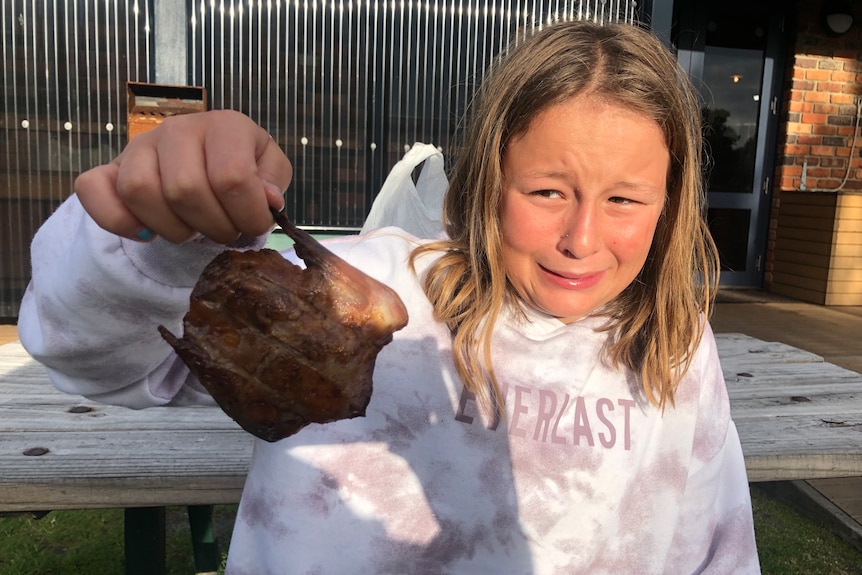 a woman screws up her face in disgust has she holds a barbecued mutton bird piece