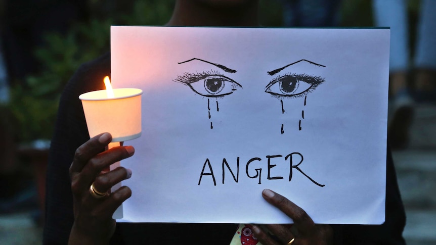 A woman holds a candle and placard reading "anger".