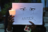 A woman holds a candle and placard reading "anger".