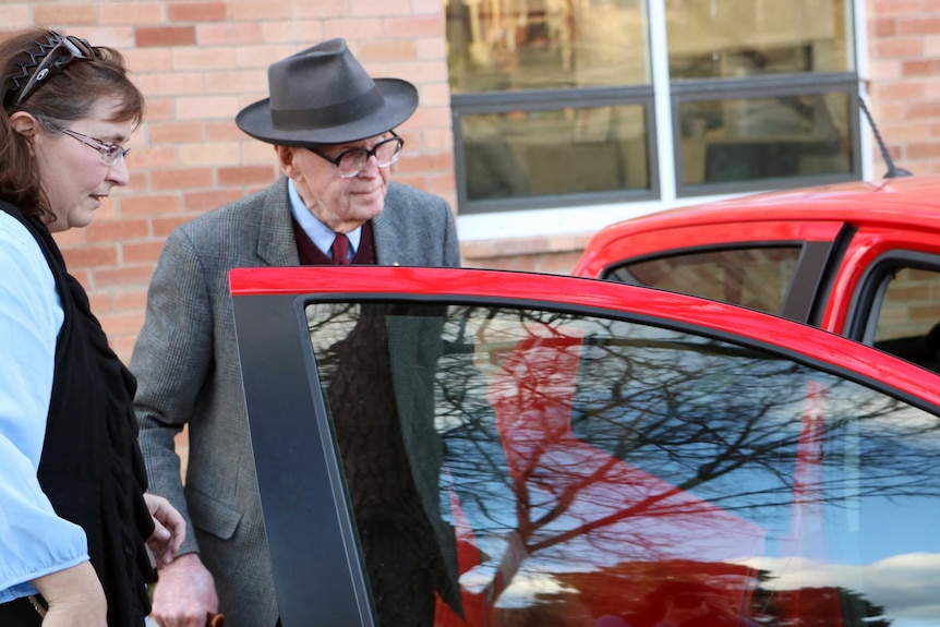 A woman and an elderly man about to hop into a red car.