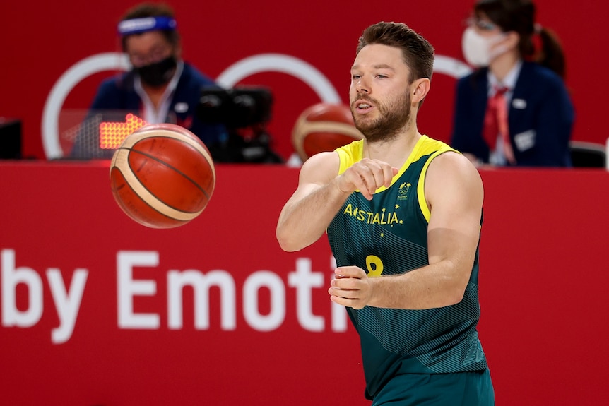 An Australian male basketball player passes the ball to his left at the Tokyo Olympics.