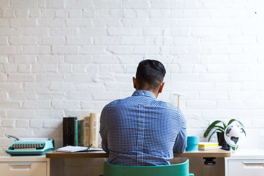 Man in a blue checkered shirt sitting at a work desk for a story about barriers culturally diverse people face at work