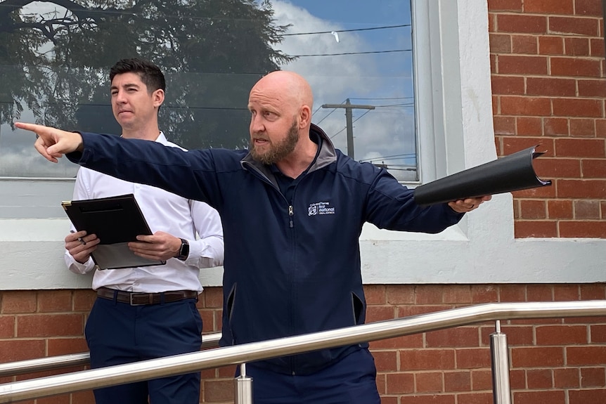 A bearded man with a shaved head points as he conducts an auction.