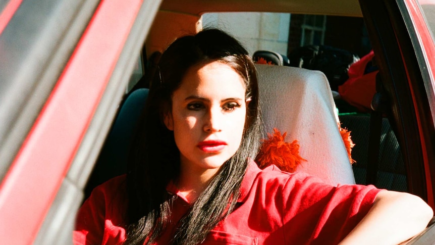 sofia kourtesis wearing a red polo shirt, sitting in a red car with the window down and the sun shining on her face