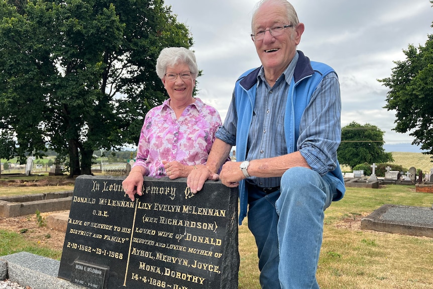  An elderly man and woman stand by a headstone