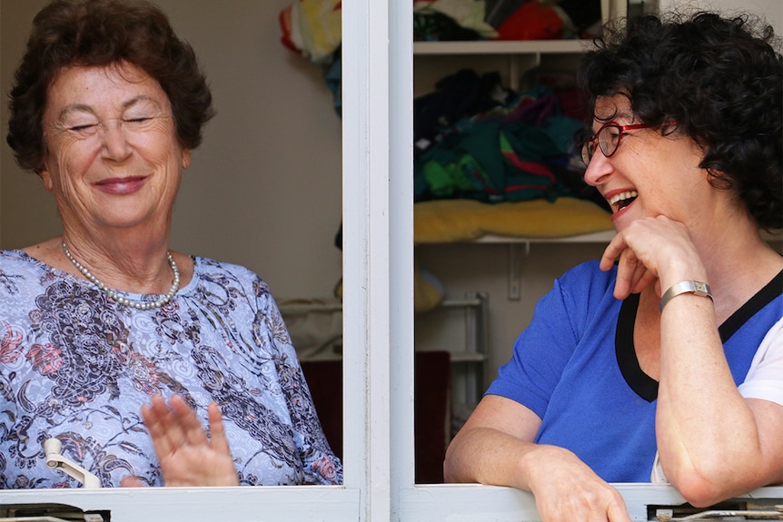 Two women laugh, viewed through a window.