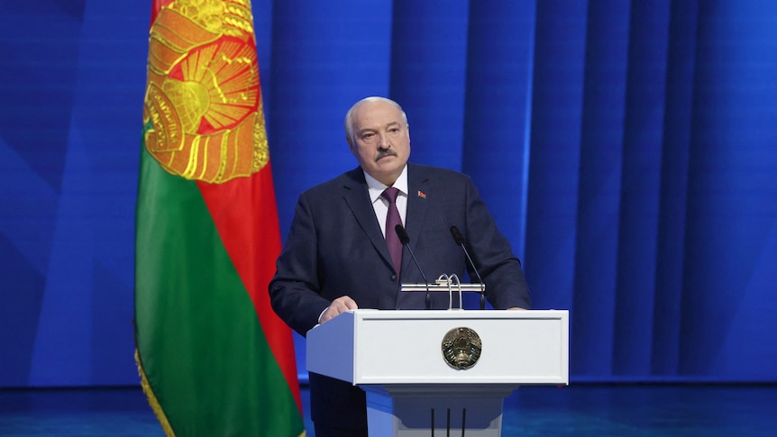 Lukashenko stands at a podium with the Belarus flag behind him, 