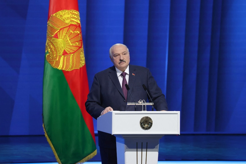 Lukashenko stands at a podium with the Belarus flag behind him, 