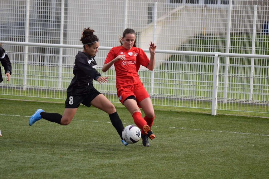 A French Tunisian female soccer player runs with the ball at her feet as a defender tries to intercept her.