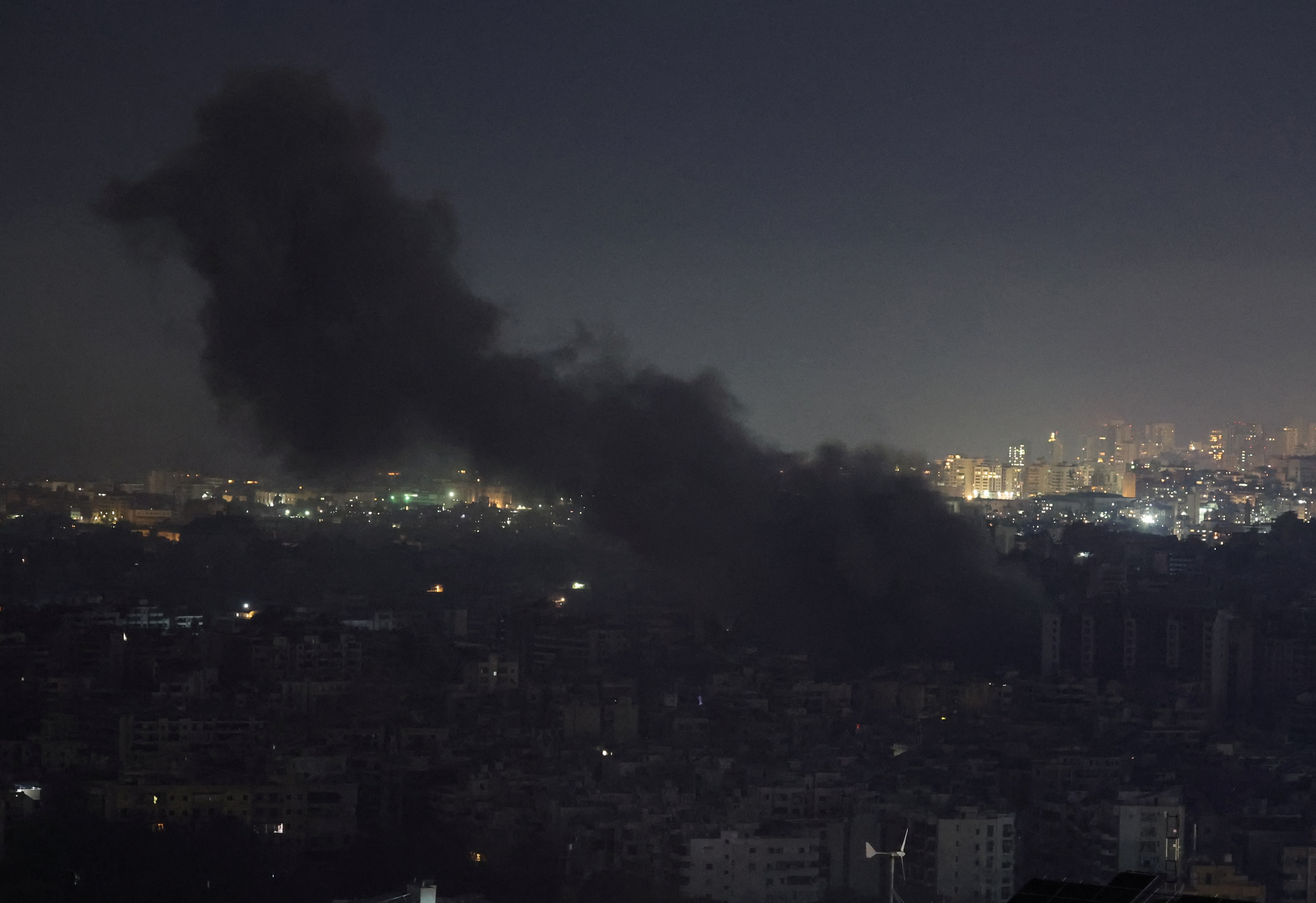 A plume of smoke rises at night over a city.