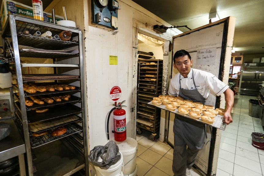 Chan Khun walking out of the cool room carrying a tray of pies.