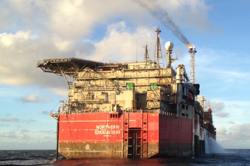 a large oil vessel on the water with smoke coming out of a flare on the front.