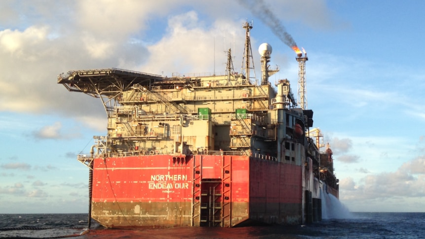 A large oil vessel on the water with smoke coming out of a flare on the front.