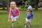 Two little girls play on the grass in the park.
