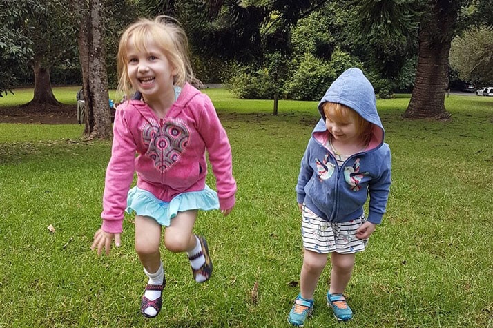 Two little girls play on the grass in the park.