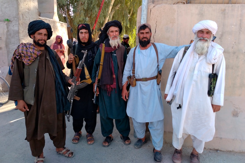 Taliban fighters pose for a photo with guns slung across their backs after taking over Farah city